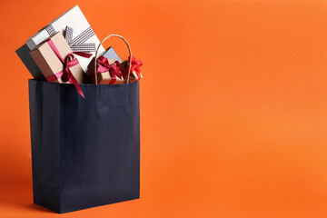 Dark blue paper shopping bag full of gift boxes on orange background. Space for text © New Africa