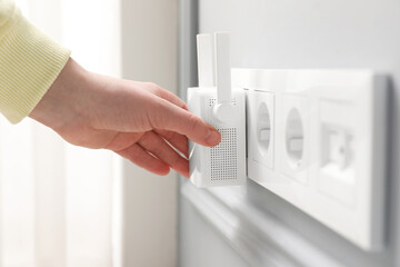 Woman turning on wireless Wi-Fi repeater indoors, closeup