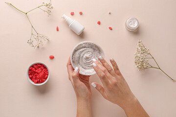 Female hands with jar of body scrub, cosmetic products, sea salt and gypsophila flowers on color...