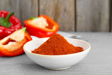 Bowl with aromatic paprika powder and fresh bell peppers on grey wooden table