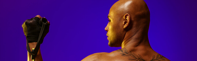 Back view of sporty man with naked torso performs exercises with expander on studio background