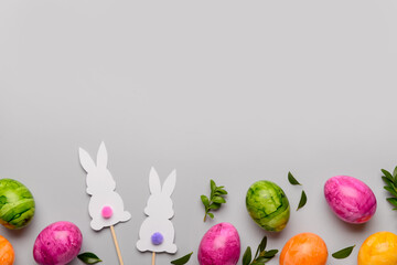 Composition with Easter eggs, paper bunnies and plant leaves on grey background