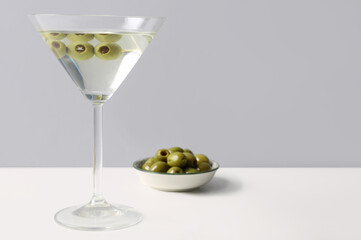 Glass of martini and olives on light background