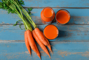 Glasses of fresh carrot juice on blue wooden background