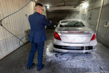 Male wash the car with high pressure washer. Car wash with foam in car wash station. A man sprays...