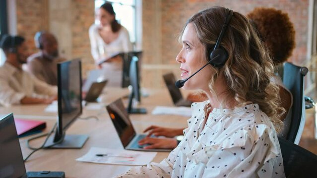Businesswoman in multi-cultural business team wearing headsets in customer support centre - shot in slow motion