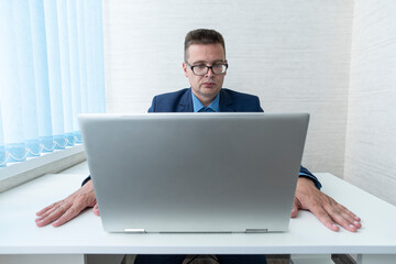 employee looking wearing glasses at computer monitor during working day in office. focused reading of information on a laptop in the office. The manager is at work.
