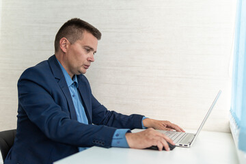 young man in a blue jacket is working on a laptop at home in quarantine. Businessman and remote business. Remote work.