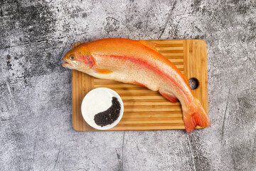 Raw amber trout on a cutting wooden board on a dark grey background. Top view, flat lay