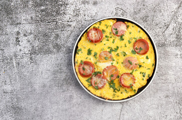 Omelet with herbs and sausage on a round plate on a dark grey background. Top view, flat lay