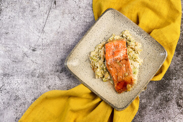 Salmon baked in cream with leeks on a square plate  on a dark gray background. Top view, flat lay