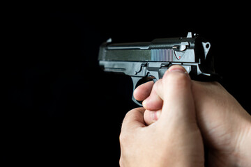 Hand holding a gun, on black background. concept of the crime of banditry. A dangerous shooter and a black pistol on a dark background. The hired killer is preparing to shoot.
