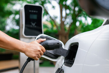 Hand inserting EV charging plug to electric vehicle in focus shot with blurred background of...