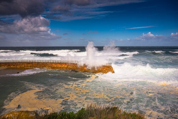 2023-02-22 THE CHILDRENS POOL AND WALKWAY DURING A STOREM WITH WAVES CRASHING AND SPRAYING AND A BRIGHT SKY
