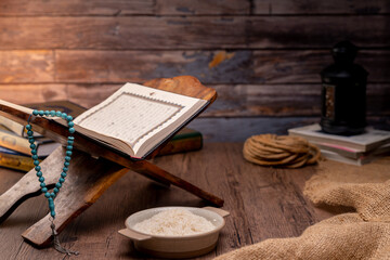 Fototapeta na wymiar Holy Quran and a grain of rice in a wooden bowl in the sack on a wooden table, Islamic zakat concept. Muslims to help the poor and needy. Conceptual shoot for property, income, and fitrah zakat.