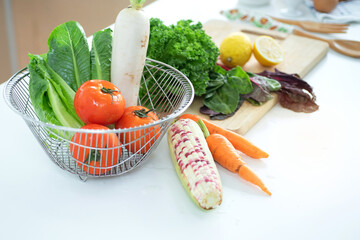 Fresh raw vegetables salad, corn,  lemon, carrot tomato, white radish and metal basket on white wood table in modern kitchen room, healthy eating concept with raw vegetable, view from above