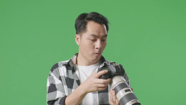 Close Up Of Asian Photographer Saying Wow After Looking At The Pictures In The Camera While Standing On Green Screen Background In The Studio
