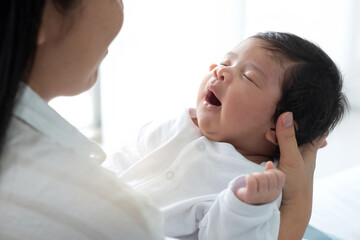 One month old newborn baby sleeps in his mother's arms and yawning, happy mum holding infant child on hands