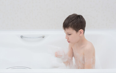 Happy boy takes a bath with lush foam playing with bubbles. Personal hygiene, healthcare concept