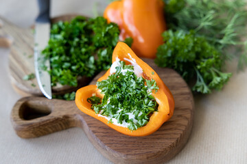 On a wooden board lies bright pepper with filling and chopped greens