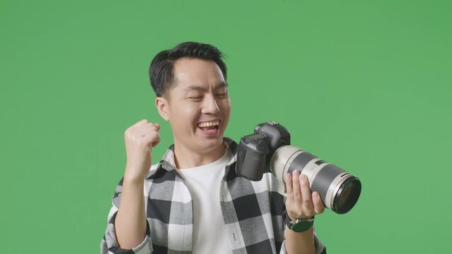 Close Up Of Asian Photographer Looking At The Pictures In The Camera Then Screaming Goal And Dancing To Celebrate Satisfied With The Result While Standing On Green Screen Background In The Studio
