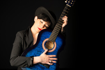 Obraz premium A young, beautiful woman in black with an acoustic blue guitar