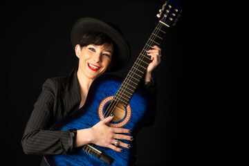 Obraz premium A young, beautiful woman in black with an acoustic blue guitar