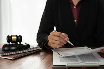 Asian woman consultant or lawyer sitting with scales and pointing with pen at signing document to read and check details of recorded data. Data justice concept.