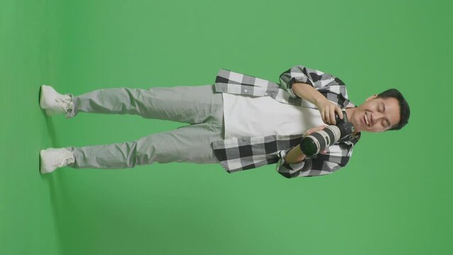 Full Body Of Asian Photographer Using A Camera Taking Pictures Then Screaming Goal And Dancing To Celebrate Satisfied With The Result While Standing On Green Screen Background In The Studio
