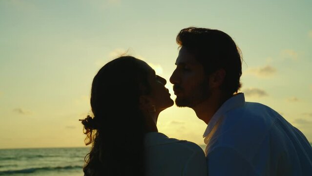 In a moment of pure romance, a young Latin couple shares a passionate kiss on the beach, the setting sun casting a warm and inviting glow over their love for each other. Romance and Lifestyle concept.