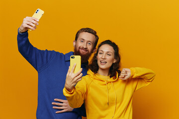 Man and woman couple smiling merrily with phone in hand social media viewing photos and videos, on yellow background, symbols signs and hand gestures, family freelancers.