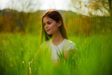 Naklejka na ściany i meble portrait of a happy woman in a white t-shirt shot through grass leaves in a field