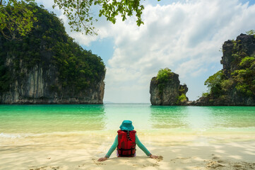 Fototapeta premium back asian child or kid girl sitting alone on beach or blue sea and wear life jacket and hat on white sand by mountain view for vacation travel on summer holiday relax at hong island krabi in thailand
