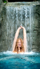 beautiful elder mature adult sexy redhead woman under the splashing water of the waterfall in the Spa Wellness pool and raises her arms