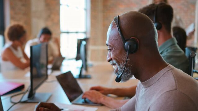 Portrait of mature businessman in multi-cultural business team wearing headsets in customer support centre - shot in slow motion