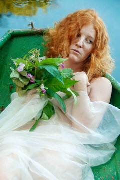 portrait of beautiful young sexy redhead girl with a sad longing and a bouquet of wilted flowers in a boat