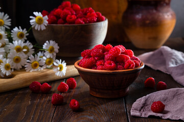 Fresh raspberries in a clay and wooden bowl on a dark wooden table