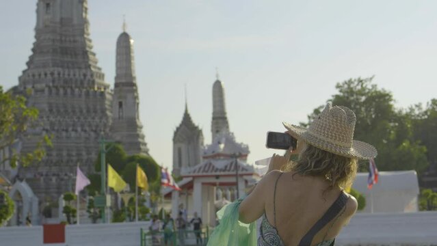 Woman tourists take pictures of the sunset at Wat Arun Ratchawararam or Wat Arun Ratchawararam. It is a popular destination for tourists around the world.
