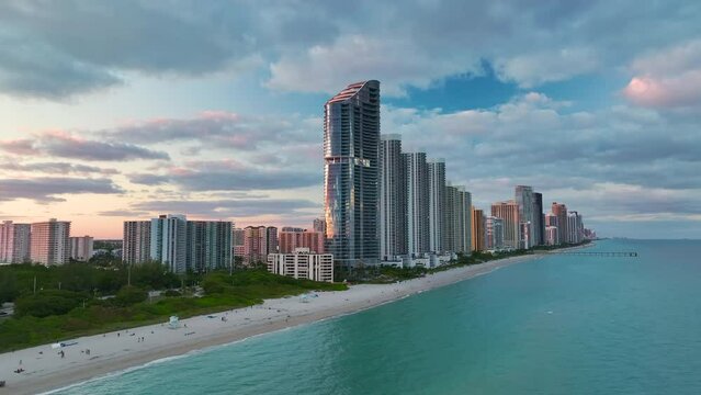 Evening landscape of sandy beachfront in Sunny Isles Beach city with luxurious highrise hotels and condo buildings on Atlantic ocean shore. American tourism infrastructure in southern Florida
