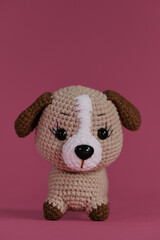 Brown little dog crocheted, handmade art. Amigurumi doll puppy on pink background. A soft DIY toy made of natural cotton and wool. Front view.