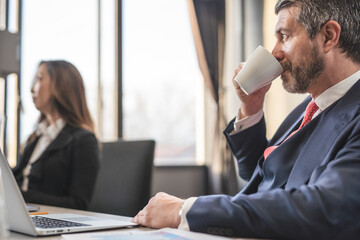 Fototapeta premium Middle-aged businessman drinking American coffee while during meeting in the office