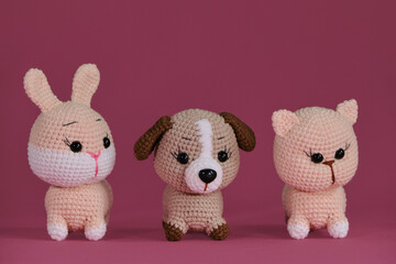 Amigurumi three pets dolls on pink background. DIY soft toys made of natural cotton and wool. Cute little kitten, puppy and rabbit crocheted, handmade art. Front view.