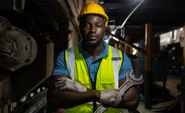 Portrait of african professional engineer stand in factory with large machines. He held a large wrench in his hand smiled with disbelief and looked at the camera in industrial worker concept.