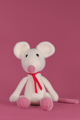 Amigurumi one white mouse with big ears and long nose on a pink background. A soft DIY toy made of natural cotton and wool. Cute little rat crocheted, handmade art. Front view.