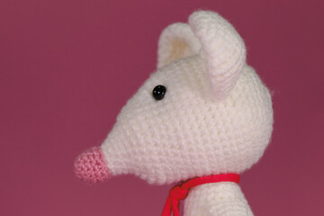 Amigurumi one white mouse with big ears and long nose on a pink background. A soft DIY toy made of natural cotton and wool. Cute little rat crocheted, handmade art. Side view, close up portrait.