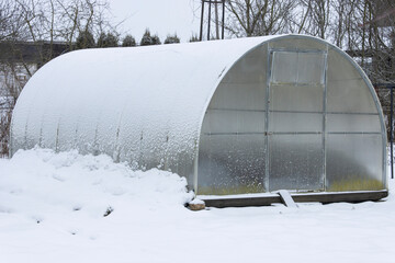 Close-up of a polycarbonate arched greenhouse covered with snow in a winter garden