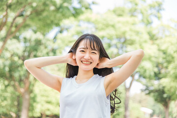新緑の中で髪を触る笑顔の日本人女性（ヘアケア・シャンプー・美髪）
