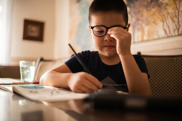 A boy with glasses draws in an album with colored pencils, eye fatigue. A glass of clean water on...