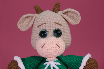 Cute little cow crocheted, handmade art. Amigurumi one brown bull wears green sweater and sits on...