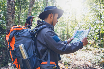 Young male traveler with backpack checks map to find directions in wilderness forest area . Tourist...